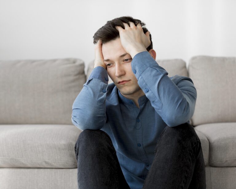 A man sitting on a sofa with his head in his hands, looking overwhelmed
