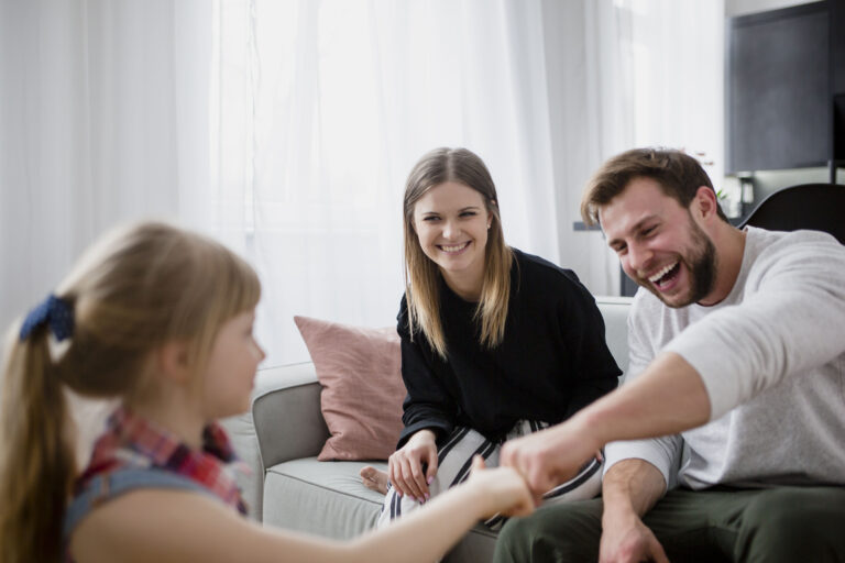 A young girl fist-bumping her smiling parents on a sofa at home