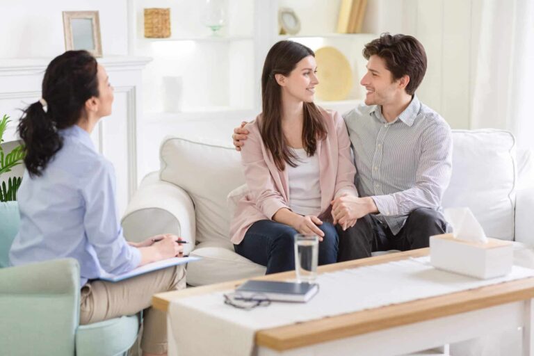 A couple sitting together and smiling during a session with their counselor